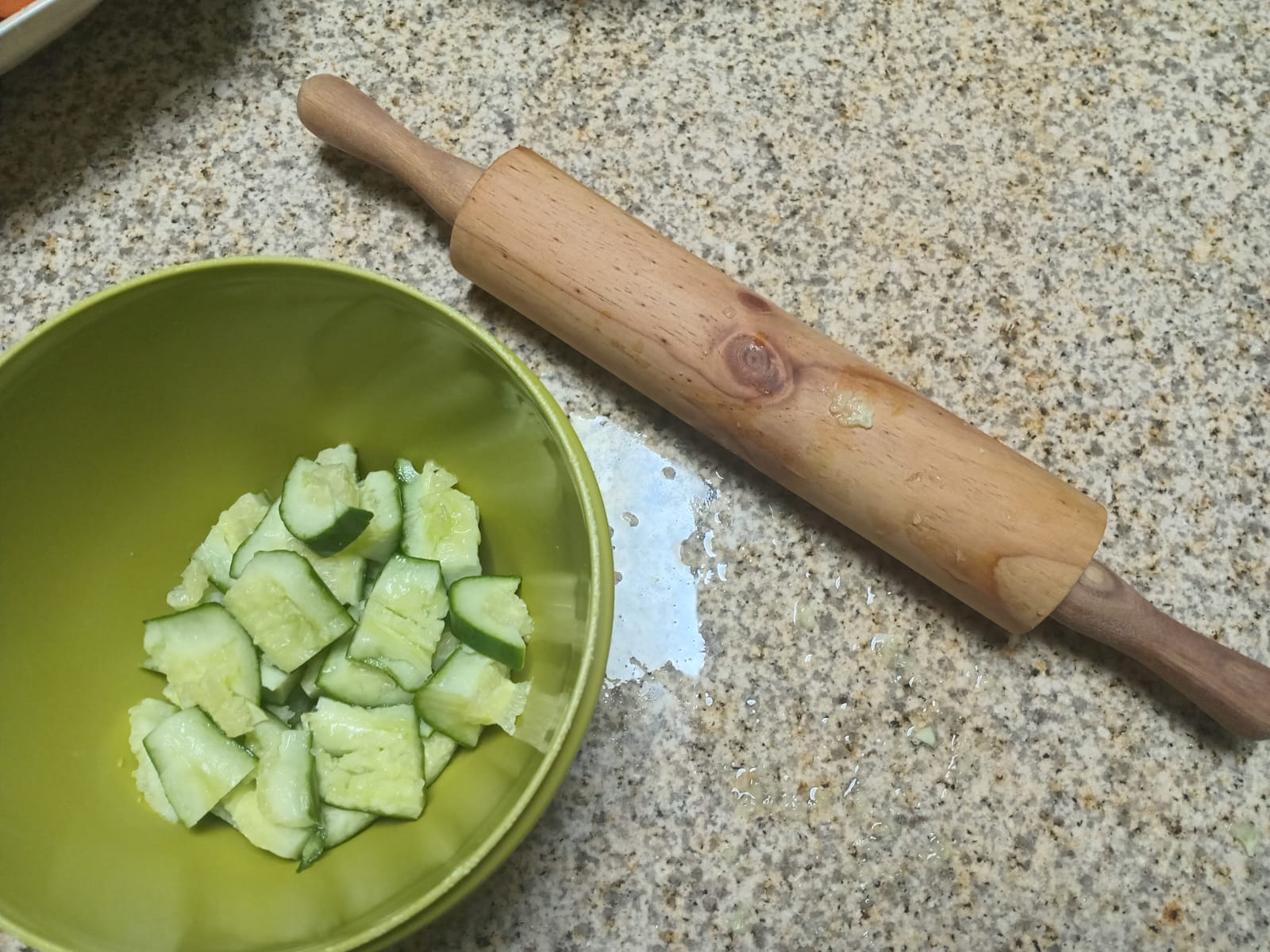 smashed cucumber pieces in a green bowl beside a rolling pin