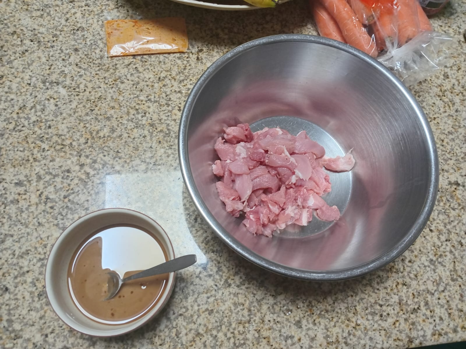 raw pork pieces in a steel bowl, the marinade still in a small bowl beside it